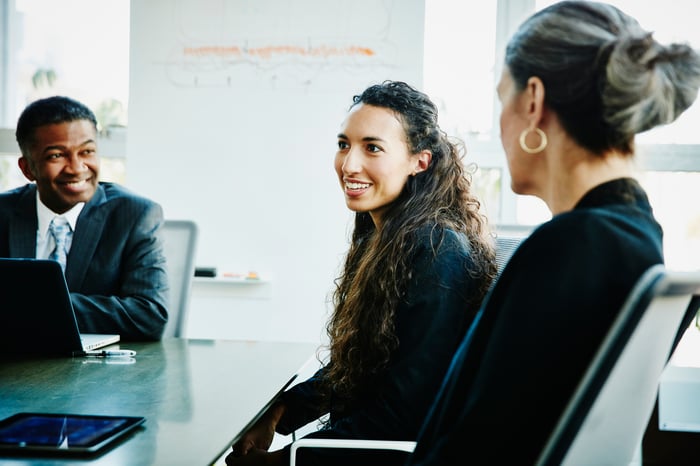 Three people in business attire seated in a conference room. 