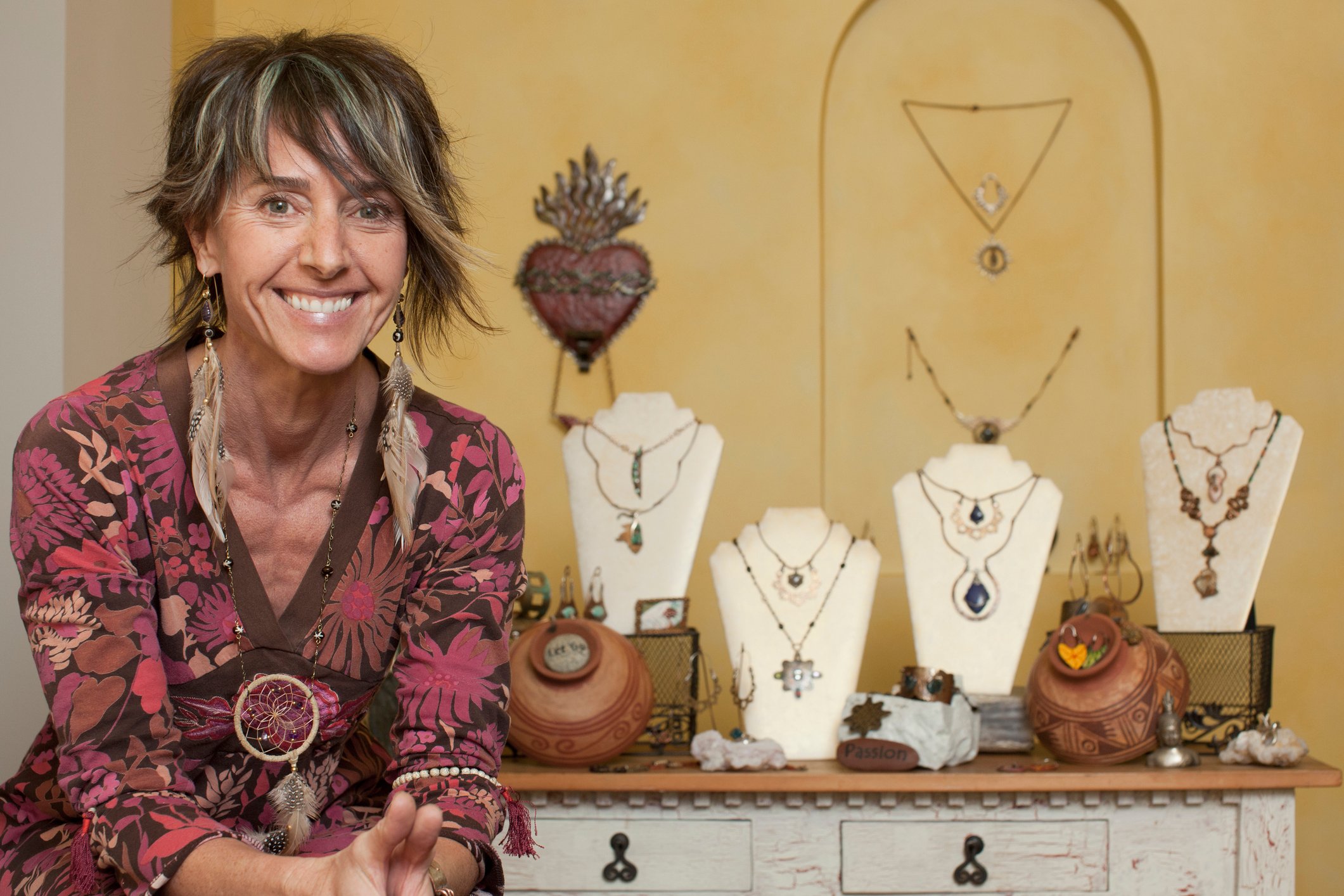 A middle aged woman smiles outside her jewelry display booth. 