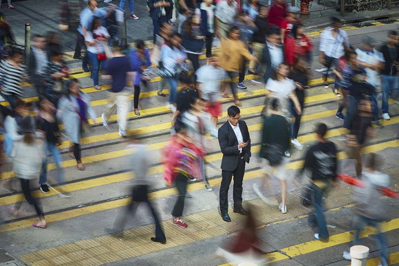 A smartphone user stands in the middle of a crowded pedestrian crossing.