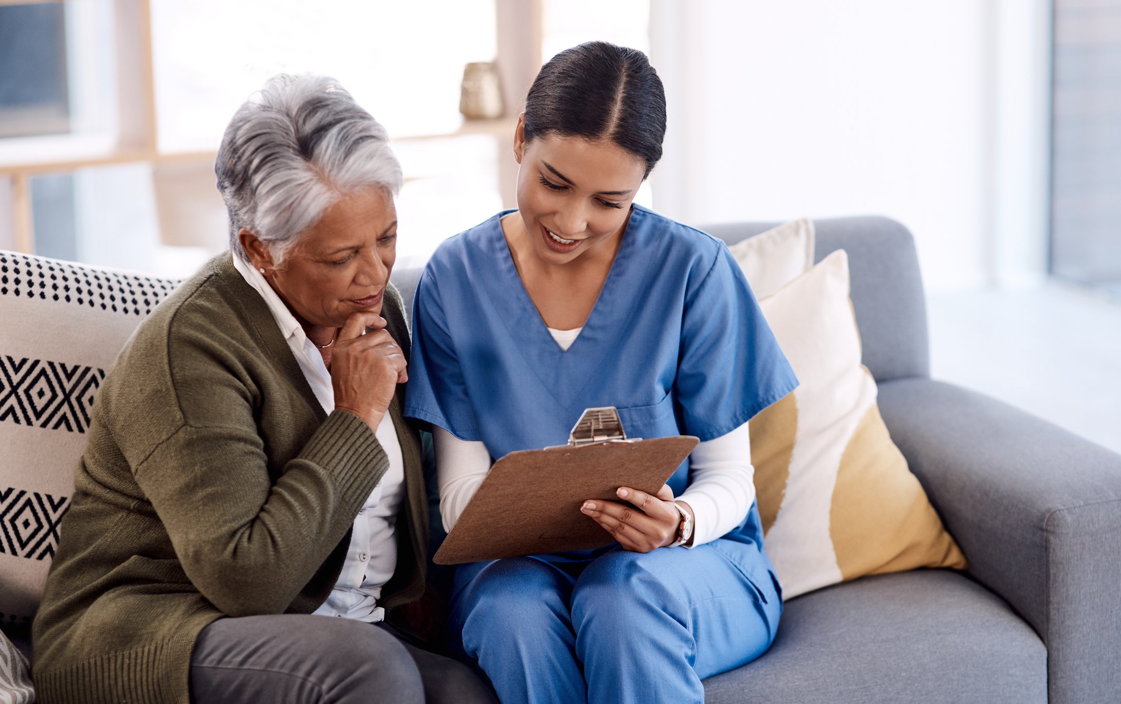 A nurse sitting on a sofa with a patient helping fill out paperwork.