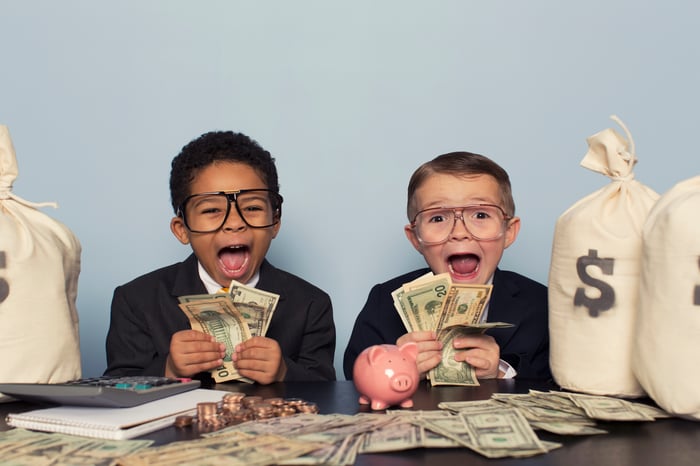 Two young children excitedly counting out a large quantity of money with money bags on the table nearby.