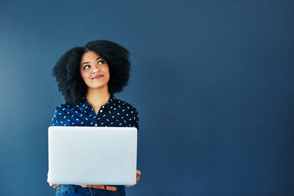 A person holding a laptop while standing against a blue background.