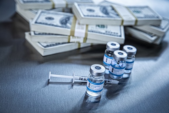 Vaccine vials with a syringe in front of stacks of $100 bills.