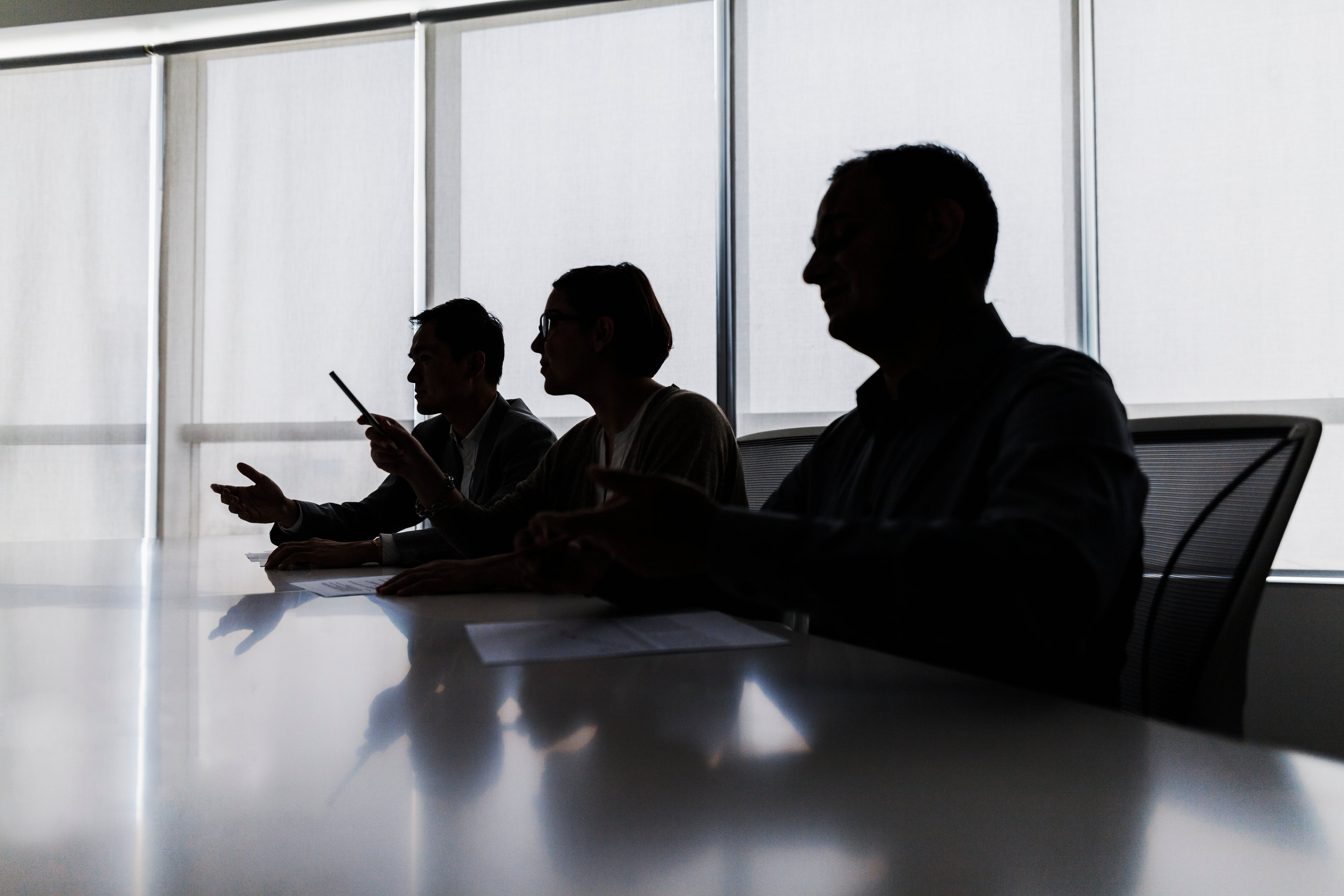 The silhouettes of three people are seen at a long table.