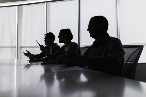 The silhouettes of three people are seen at a long table.