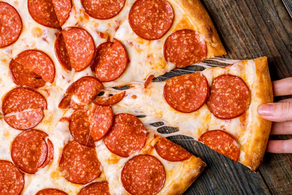 A pepperoni pizza with a hand removing one slice.