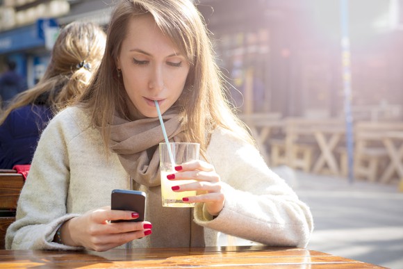 A smartphone user sips lemonade.