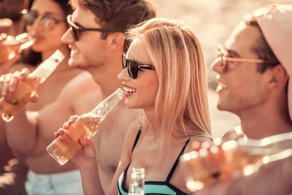 People drinking seltzer out of bottles on a beach.