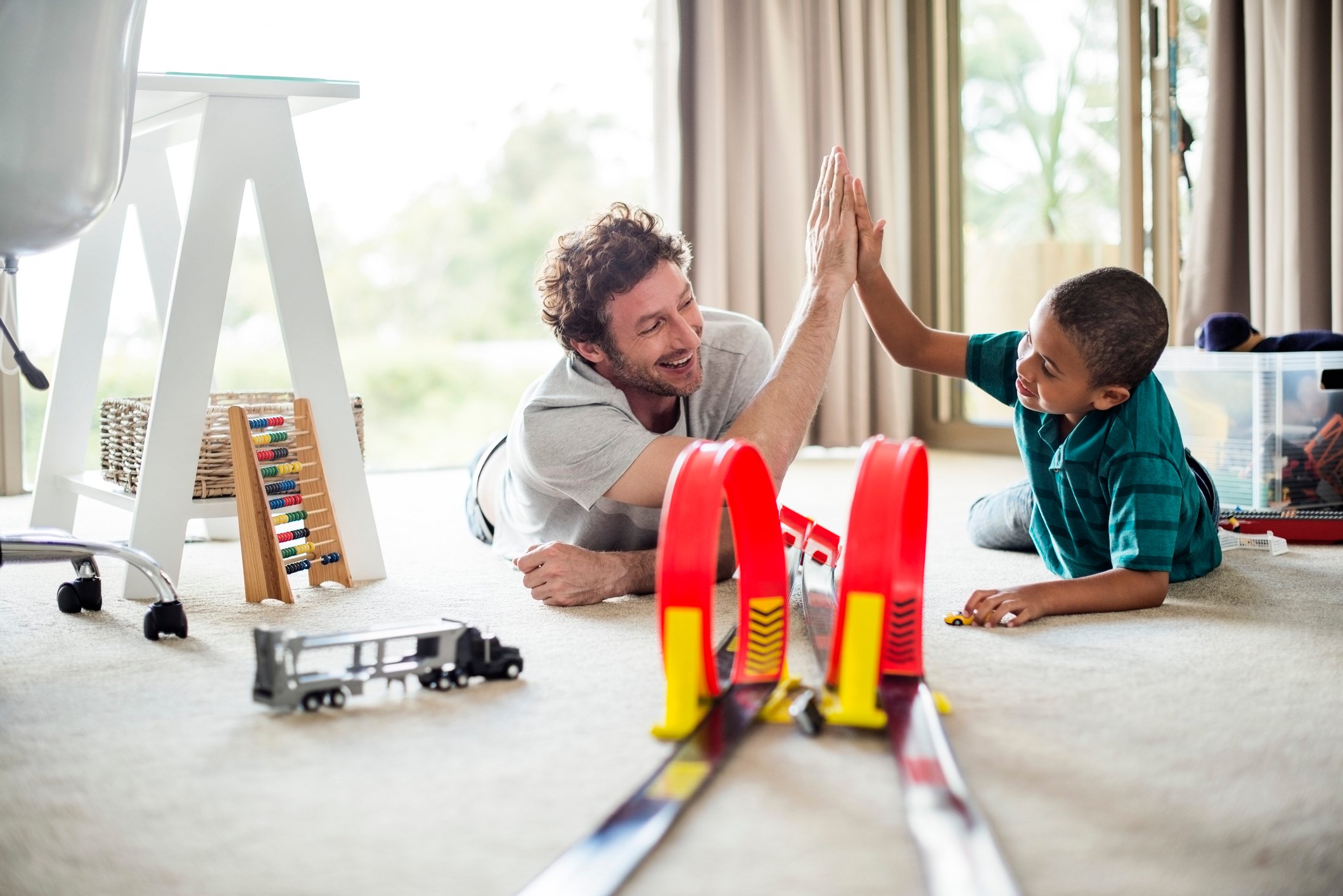 Adult and child playing with a toy race car track.