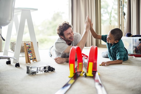Adult and child playing with a toy race car track.
