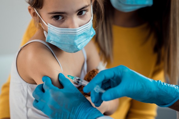 A medical professional administers a shot to a child wearing a protective face mask. 