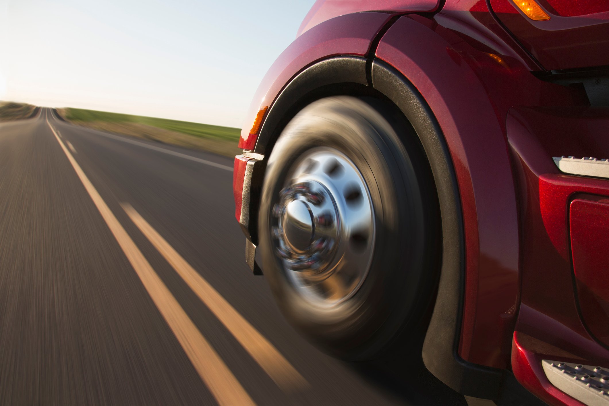 The front driver-side wheel of a truck as the vehicle barrels down a road.