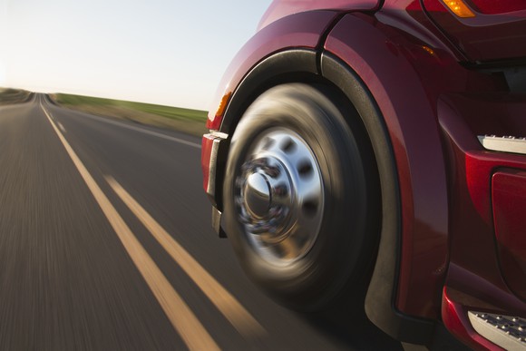 The front driver-side wheel of a truck as the vehicle barrels down a road.