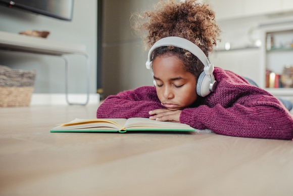 Young person frowning over a book, wearing headphones.