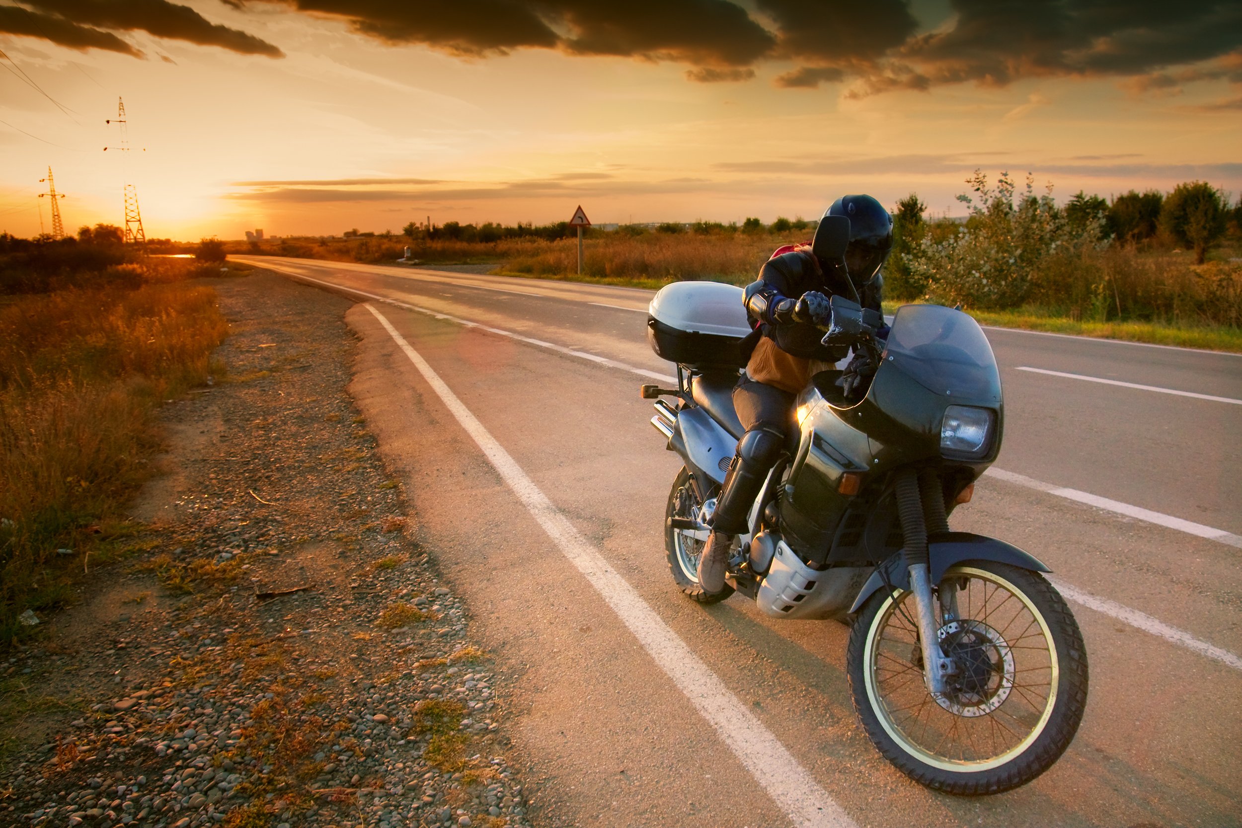 A motorcyclist on the road with the sun rising or setting in the background.