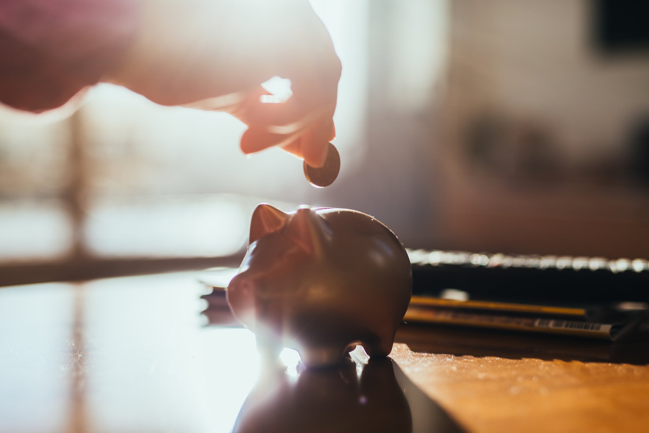 Piggy bank sitting on a table with a hand hovering over it holding a coin. 