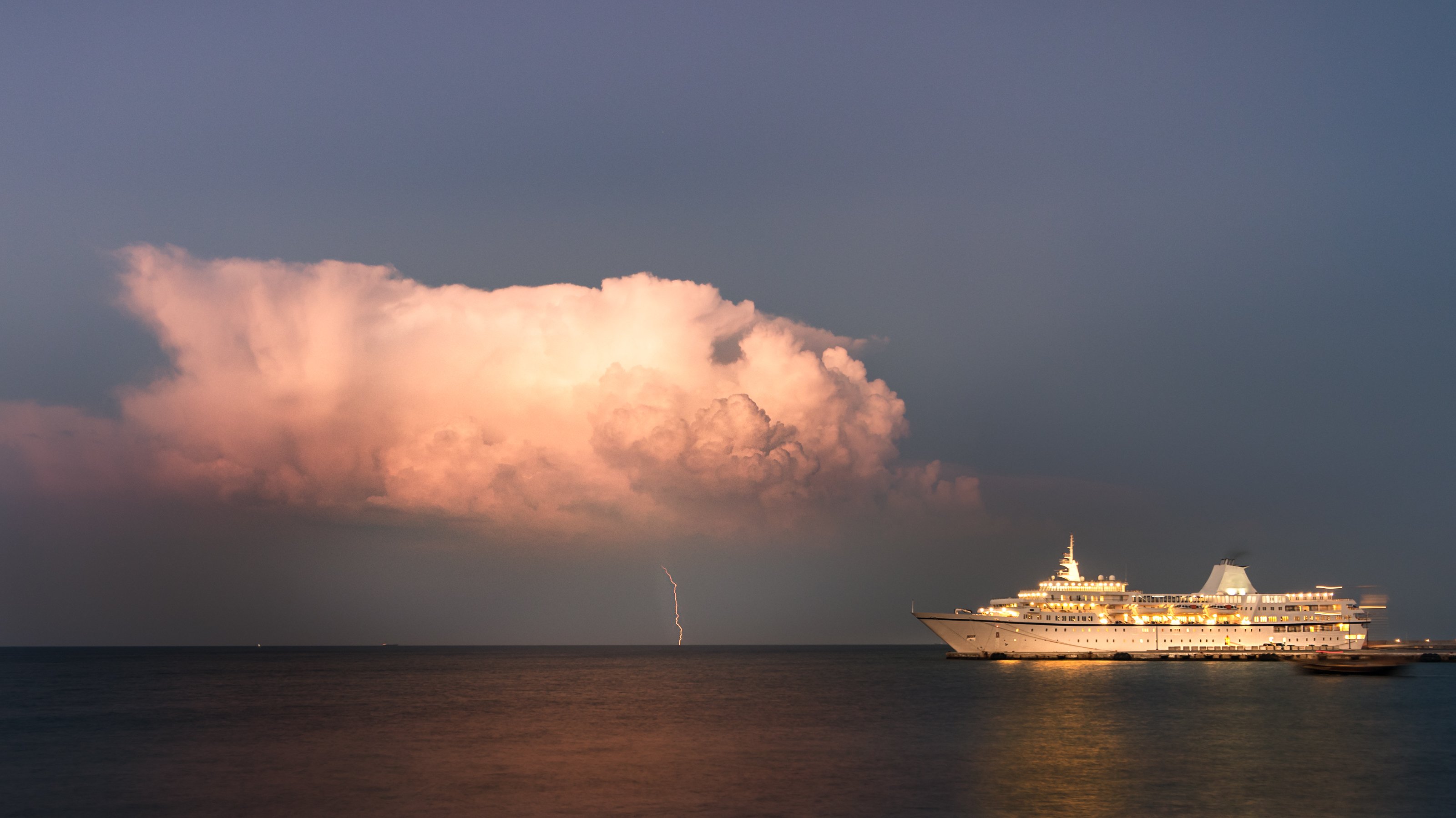 Cruise ship sailing, with storm cloud in the background.