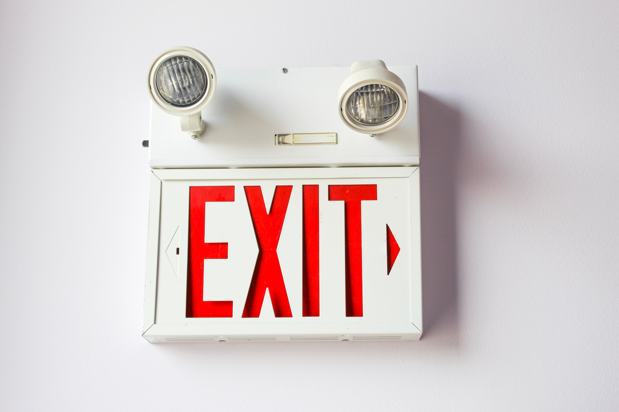 An exit sign topped with emergency lights, fixed to a wall.