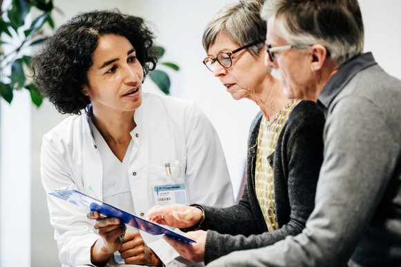 Medical professional showing information on a clipboard to two people.