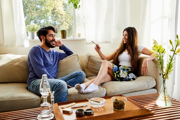 Two people on a couch in a room, with one holding a joint.