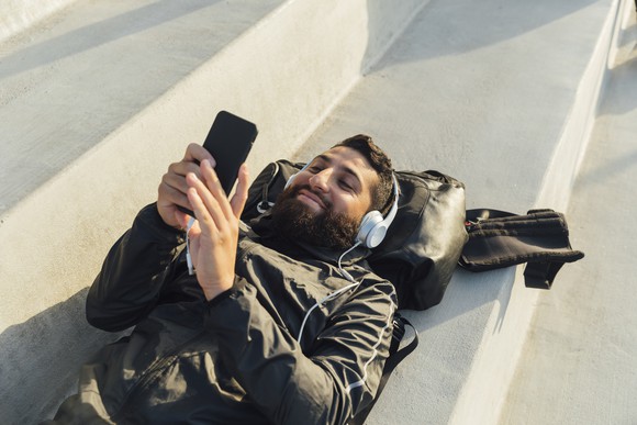 A person lying down outside listening to audio through headphones.