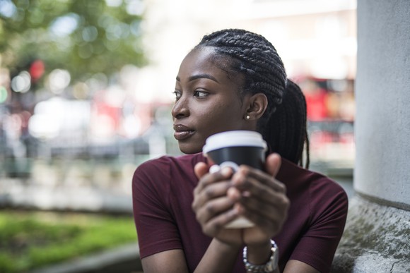A young woman drinks a coffee outside.