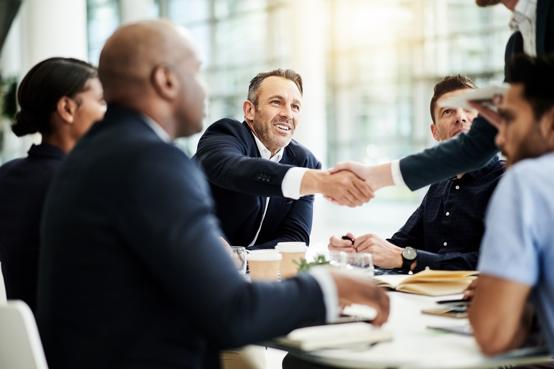 Six people gathered around a conference table while two of them shake hands.