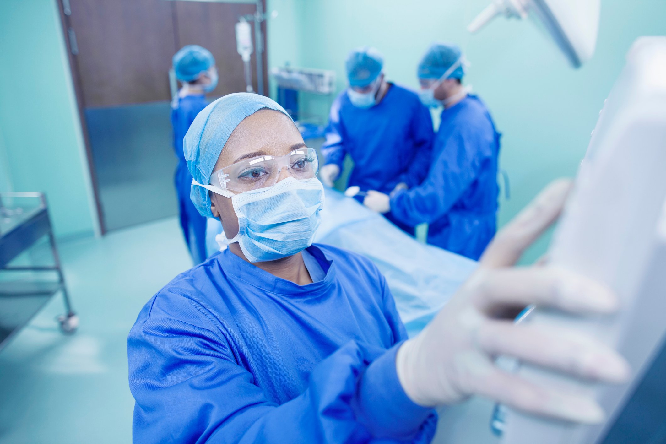 A healthcare worker operates a device inside the operating room with other members of the surgical team in the background.