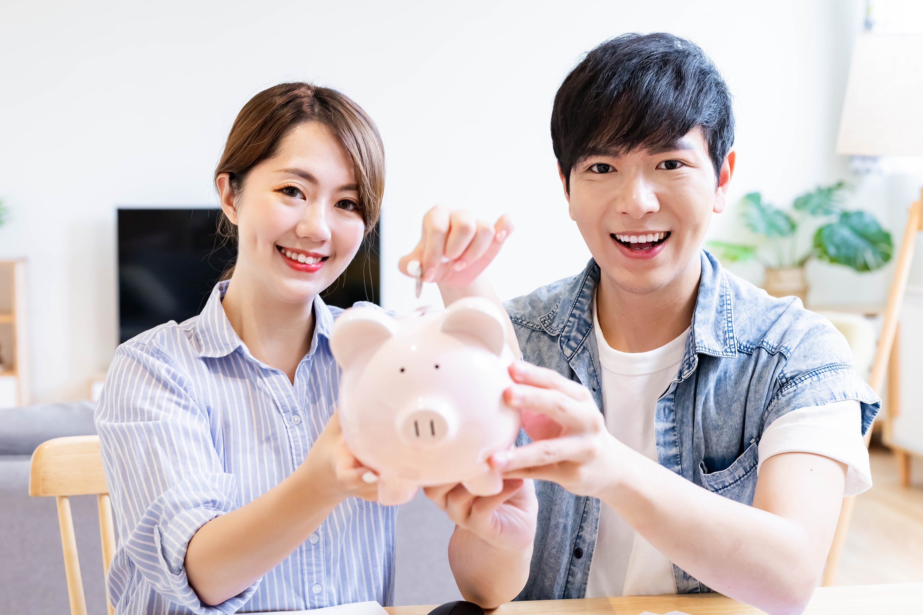 Two people putting money into a piggy bank.