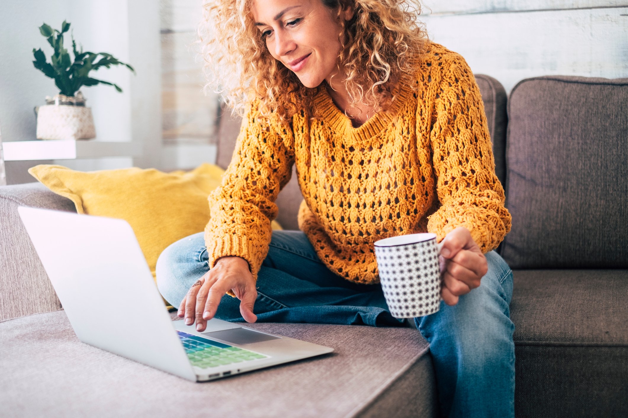 Smiling person holding coffee mug and looking at laptop.
