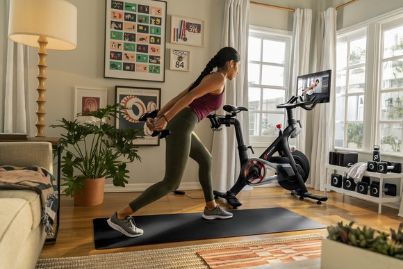 Person exercises on mat next to a Peloton Bike