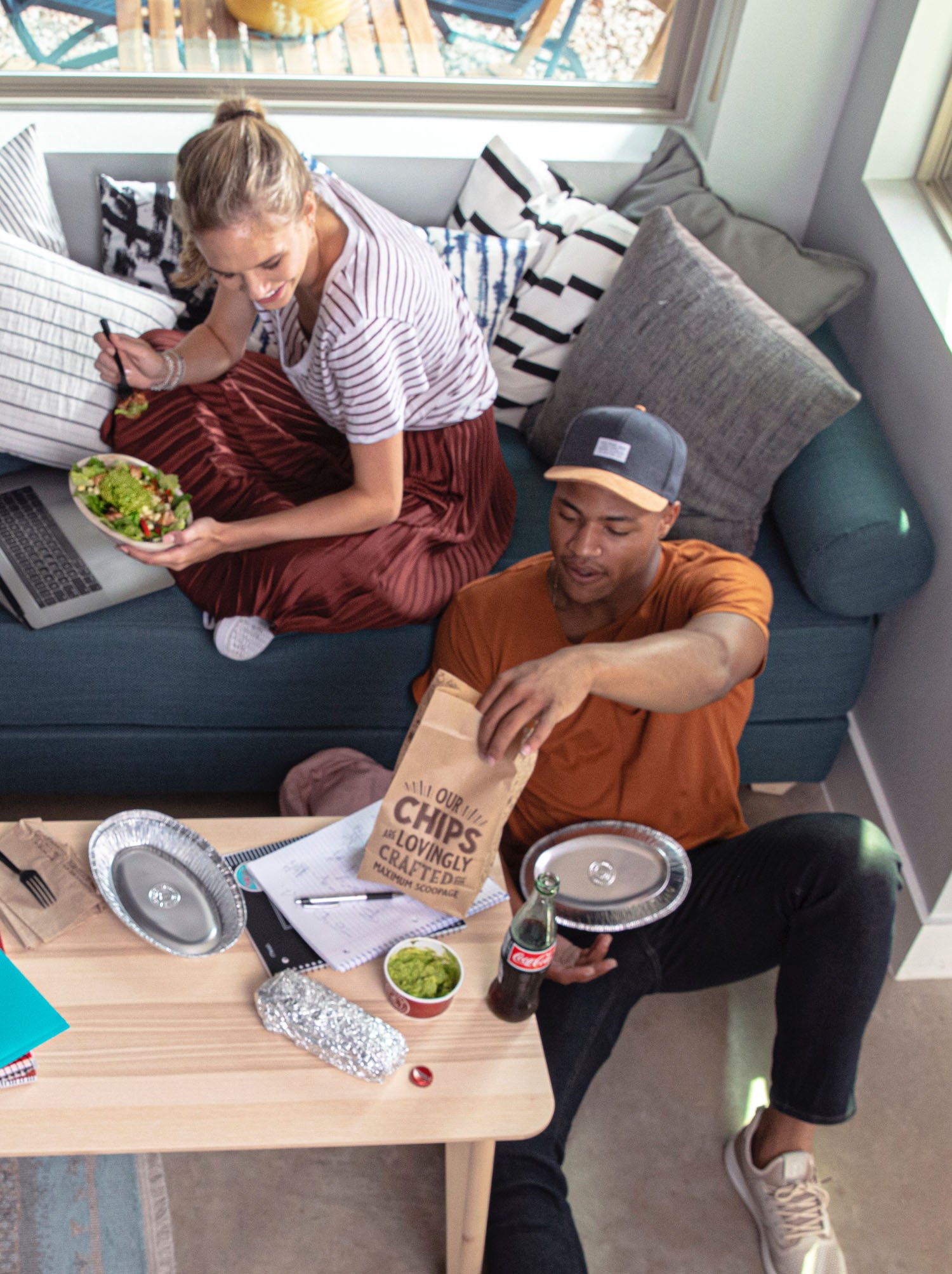 two people sitting by the couch eating Chipotle