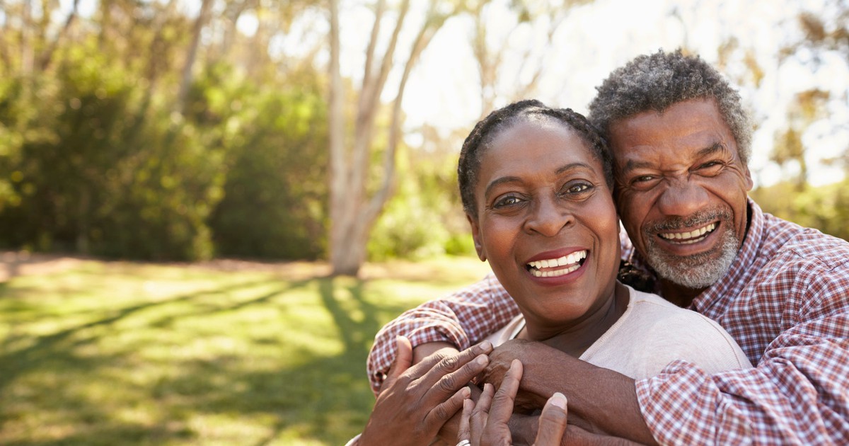 Two smiling people in an open grassy area with trees behind.