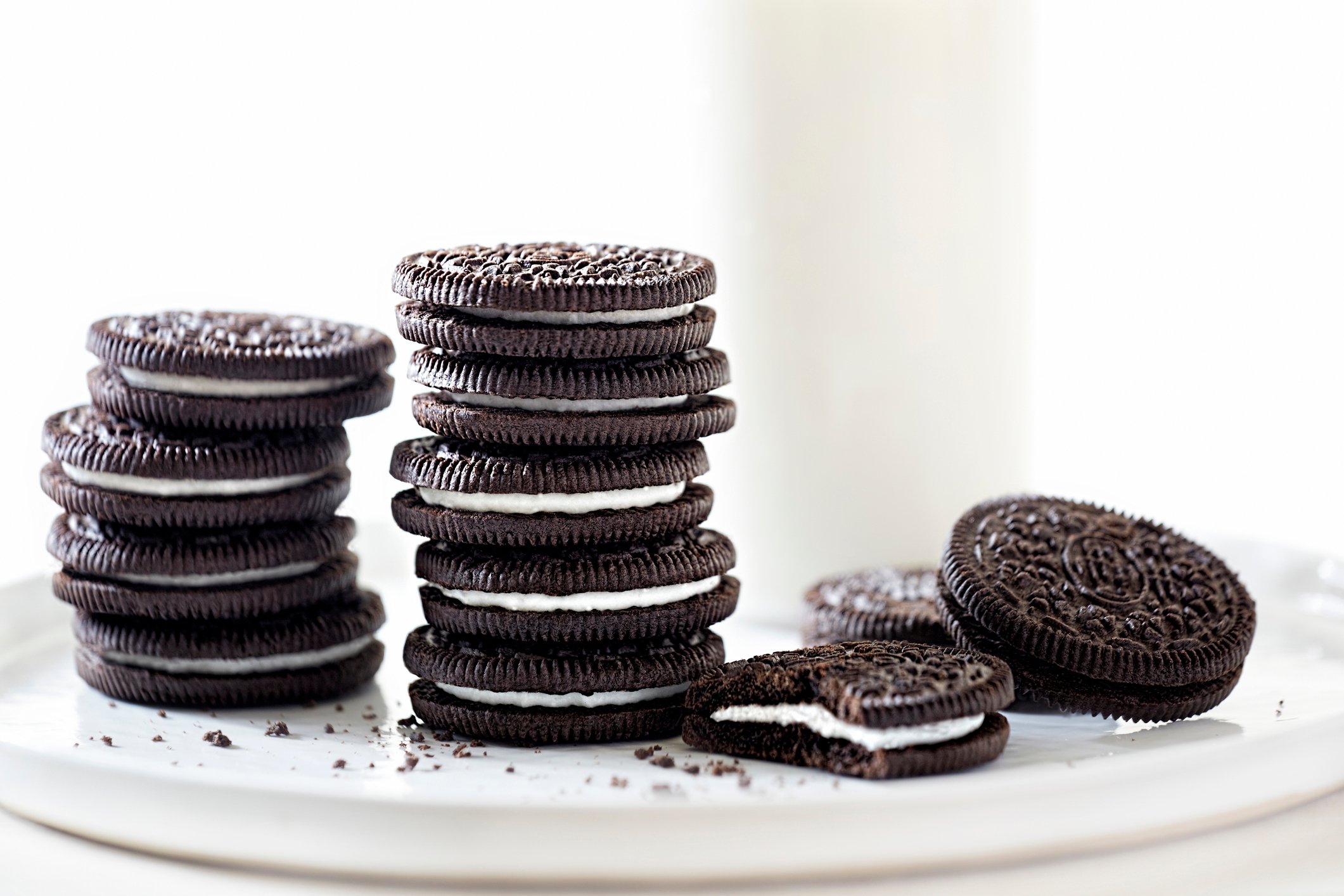 Oreo style sandwich cookies stacked on a white platter, with a glass of milk in the background.