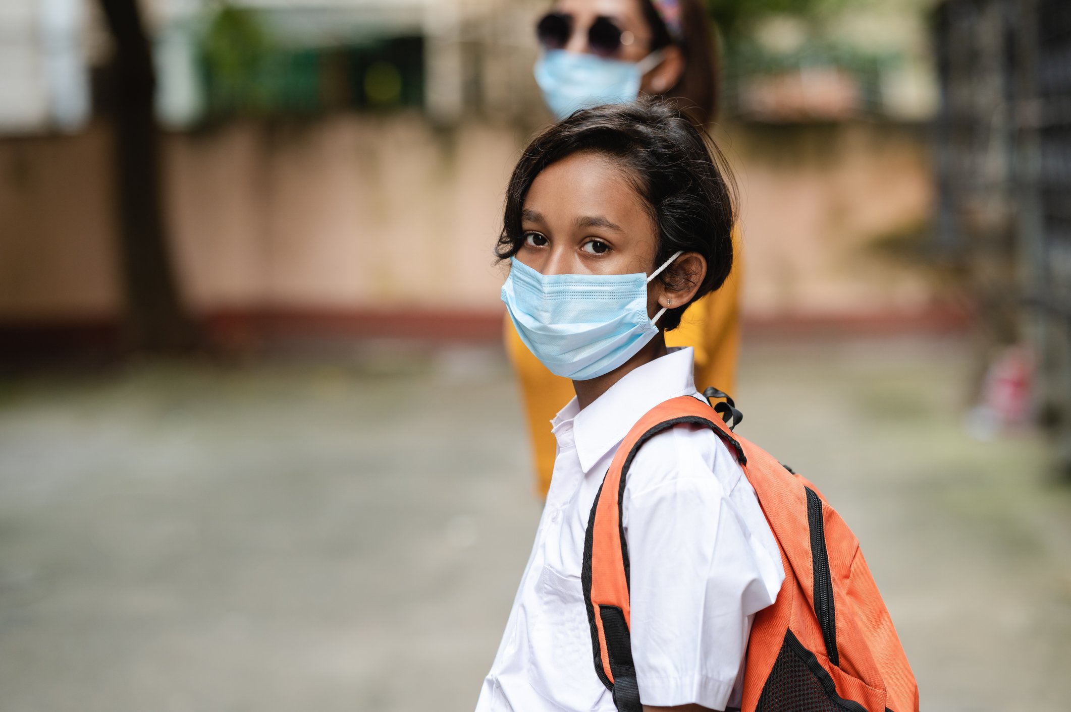 A young person wearing a backpack and a surgical mask.