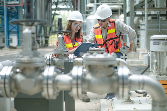 Two people wearing hard hats and safety vests inside of an energy facility.