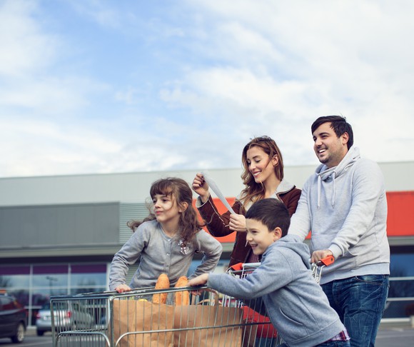 A family with a cart full of groceries in the parking lot of a store.