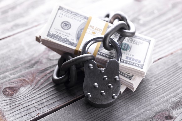 Multiple $100 bills locked up by a chain and padlock.