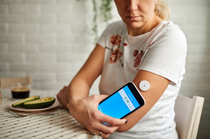 Person checking glucose level with smartphone at a kitchen table.