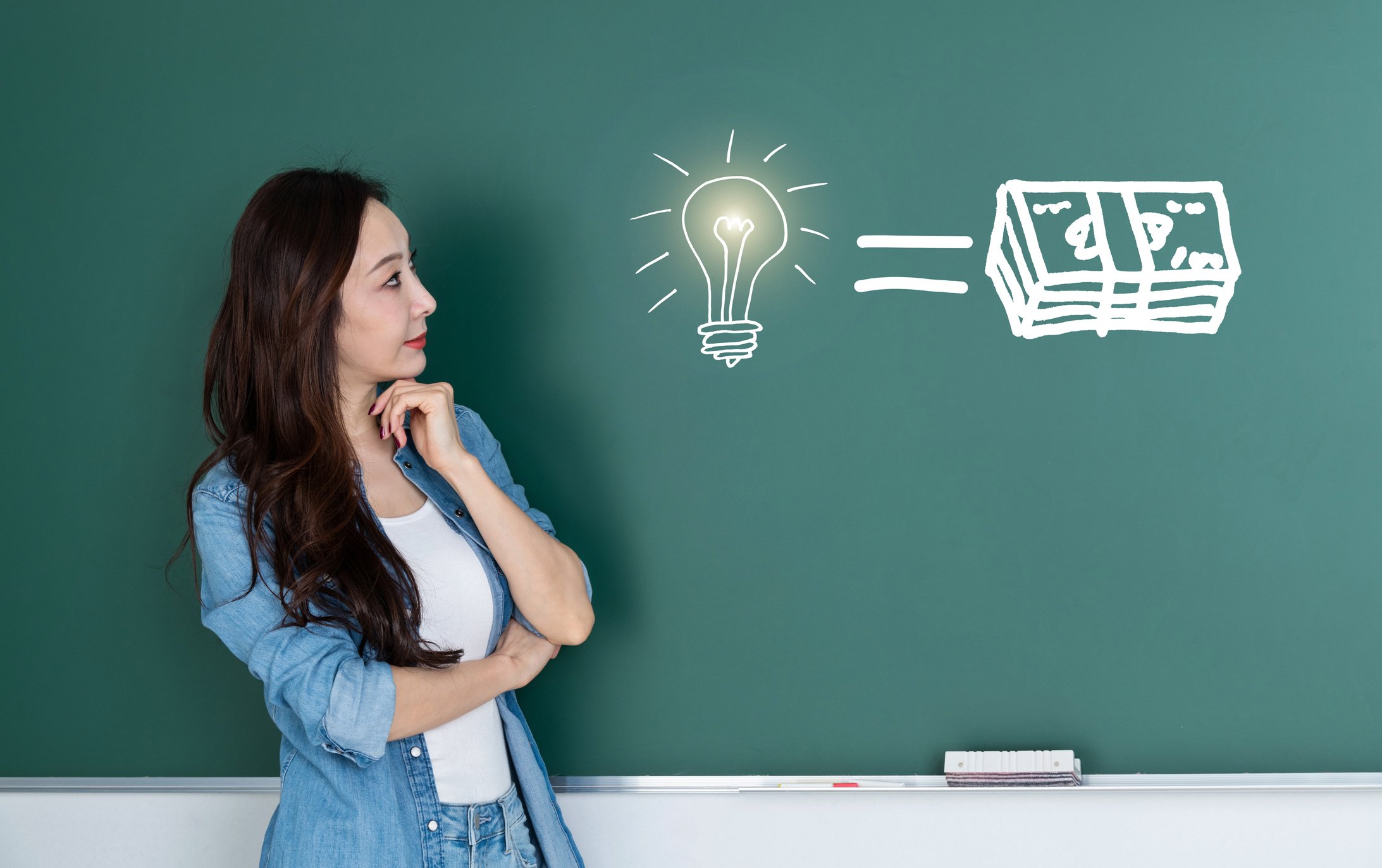 A person looking at a chalkboard drawing of a light bulb, an equal sign, and a stack of cash.