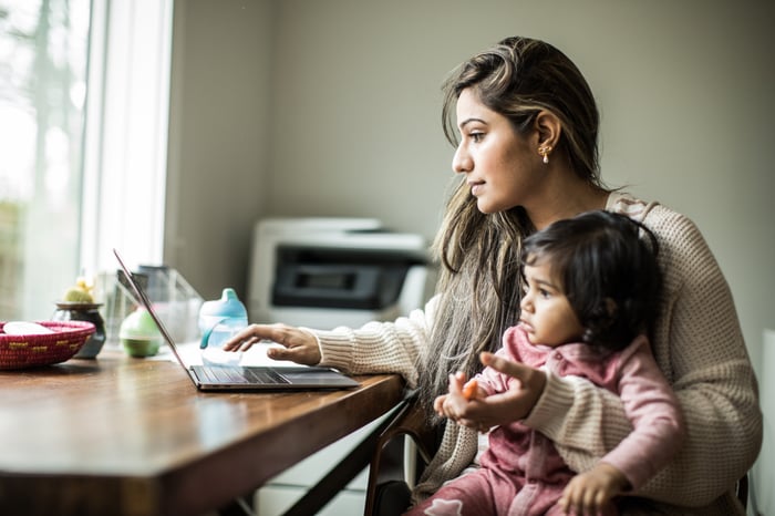 Woman working on laptop with an infant on her lap.