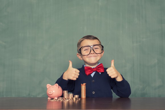 A child gives two thumbs up while putting coins in a piggy bank.