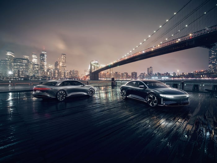 Two Lucid Air luxury electric sedans in front of bridge and city skyline at night.