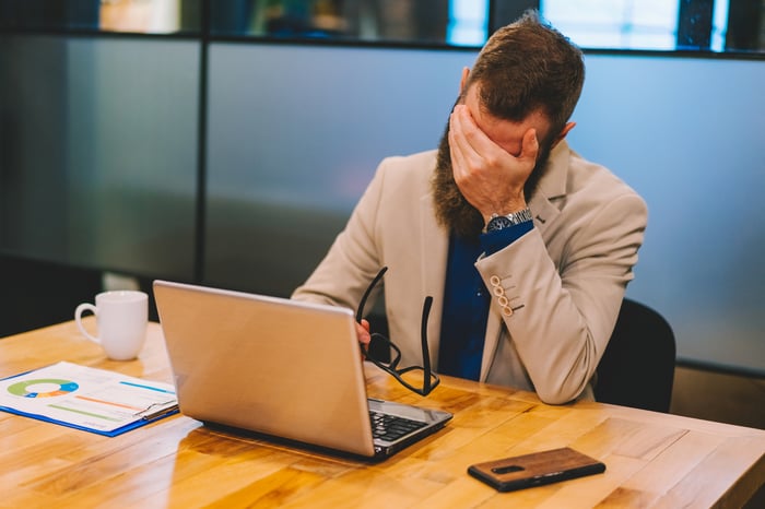 A person holding their head in their hand while sitting in front of a computer.