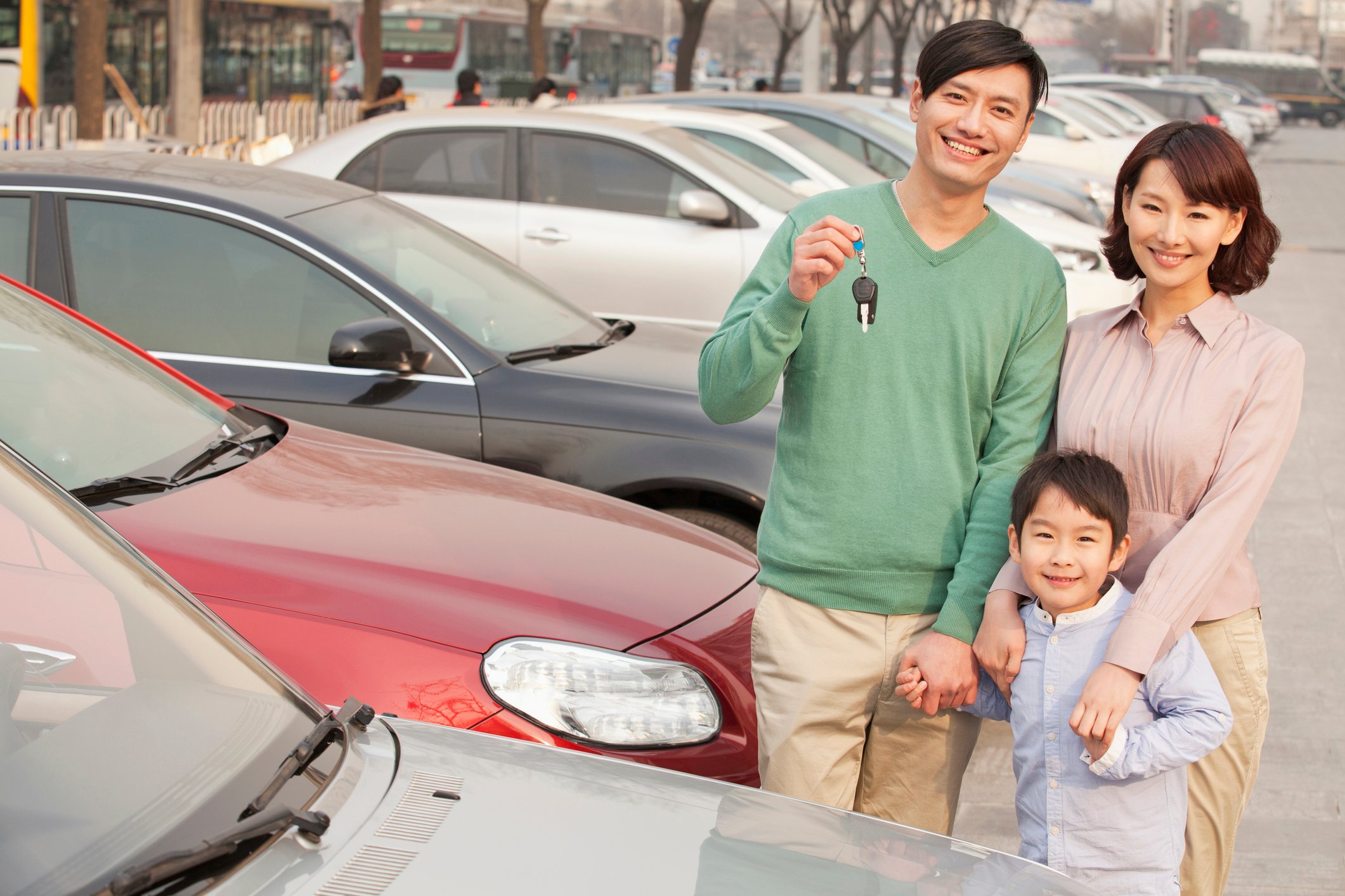 Family on car lot holding car keys.