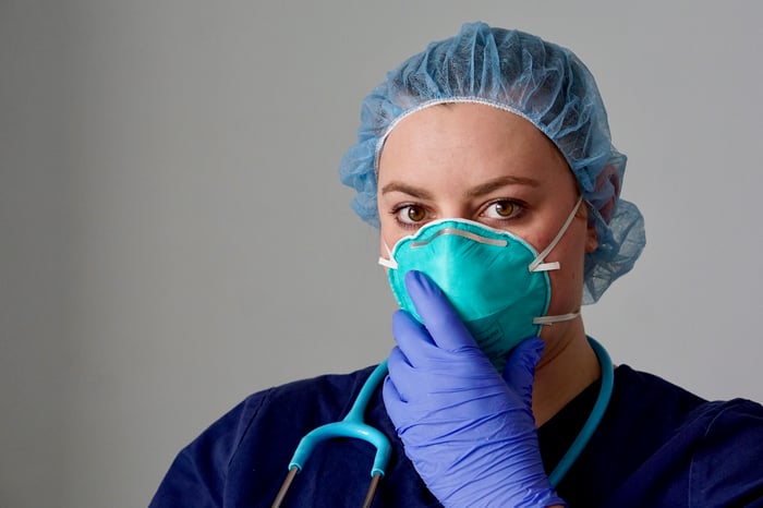 A person wearing a face mask, gloves, and a surgical hair cap.