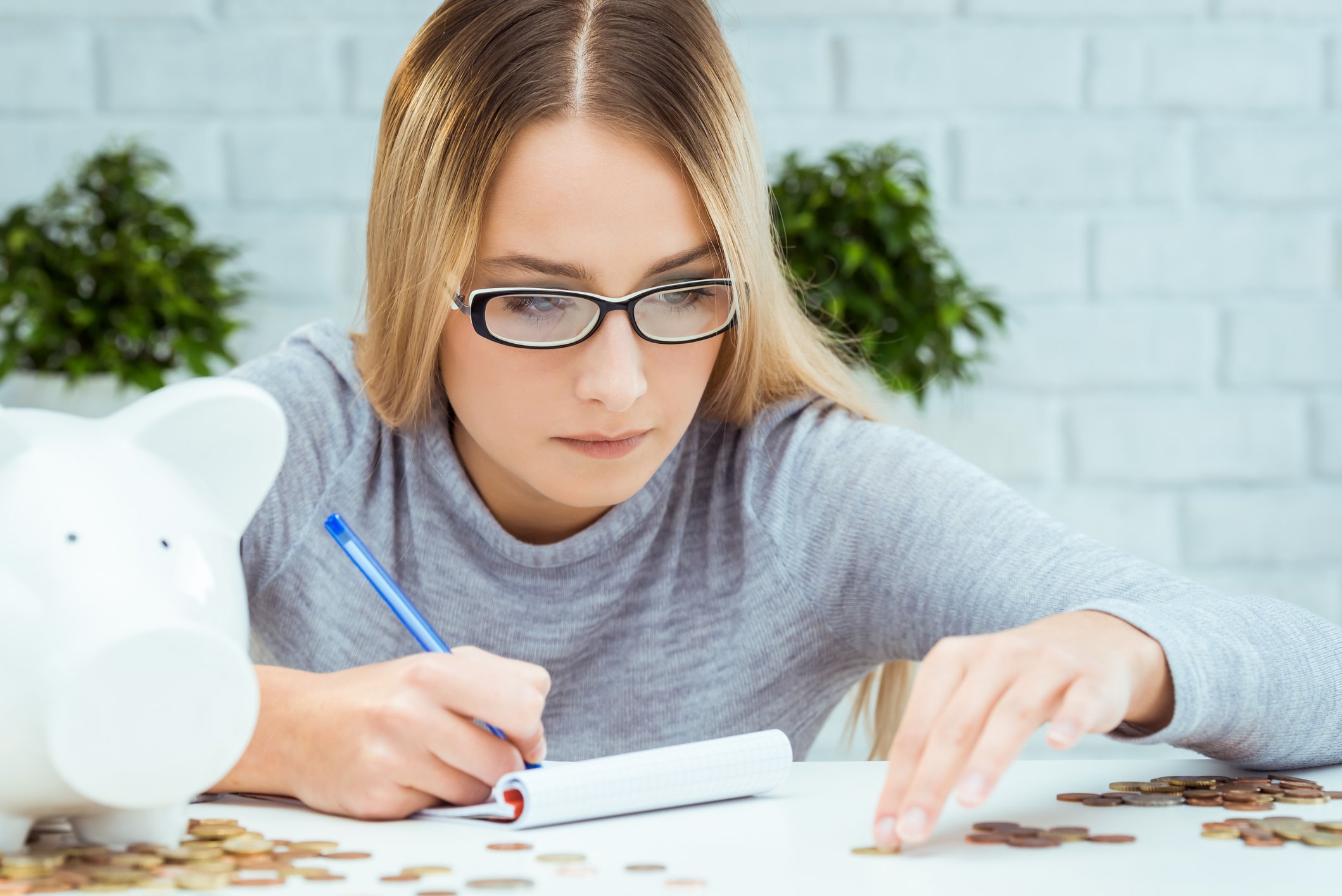 A person writing in a notebook while counting pennies from a piggybank.