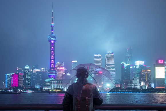 A person holding an umbrella in front of the city of Shanghai at night.