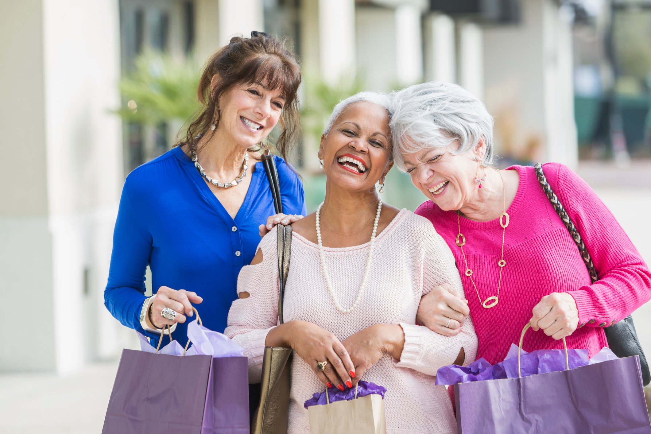 Three smiling people holding shopping bags.