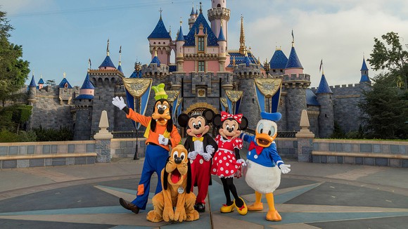 Disney costumed characters pose in front of Disneyland's iconic castle.